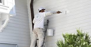 Painter on ladder, painting white siding on a house.