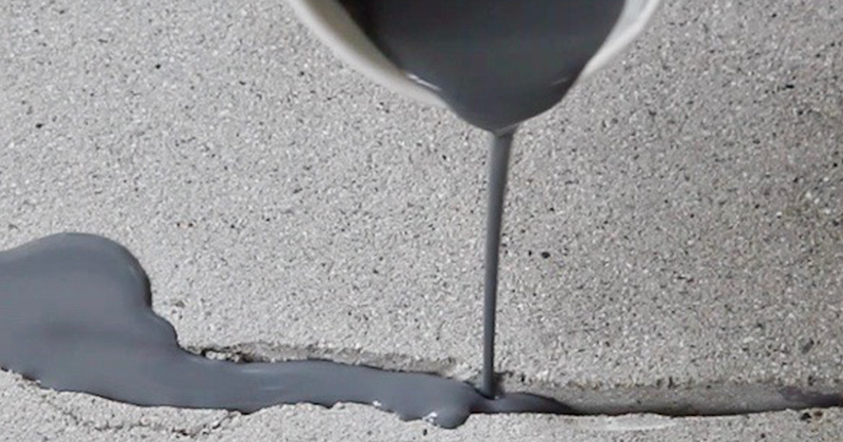 Gray liquid being poured from a white container into a crack on a concrete surface.