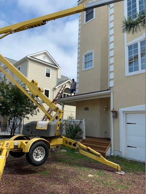 Man on roof near a yellow lift, beige house, blue sky.
