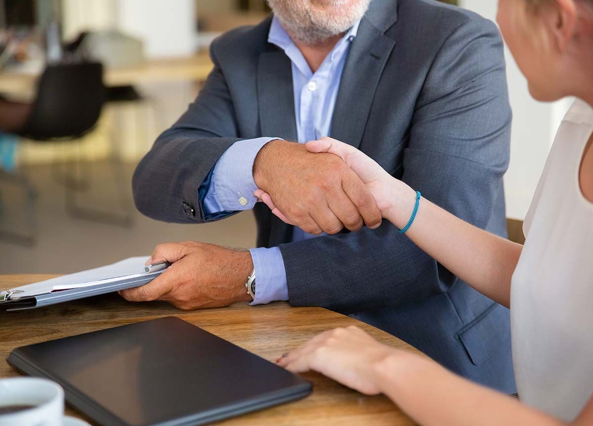 A man and a woman are shaking hands at a table.
