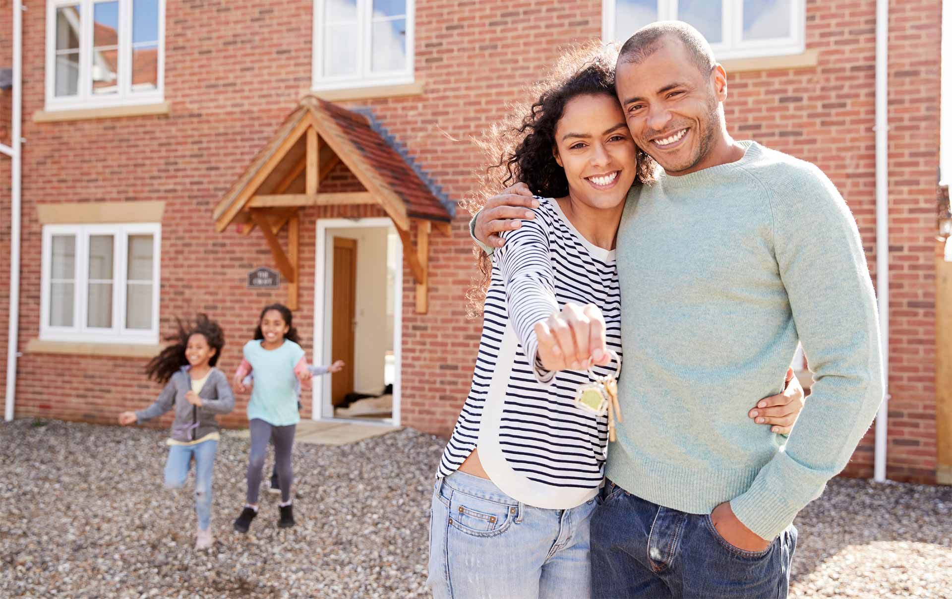 A family is standing in front of their new house holding the keys.