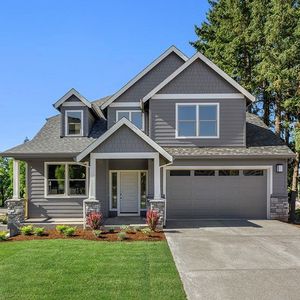 A large gray house with a large garage and a lush green lawn.