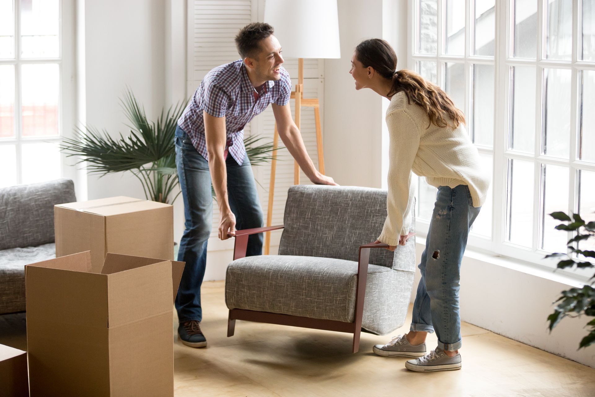 Couple moving furniture in living room, smiling, boxes nearby.