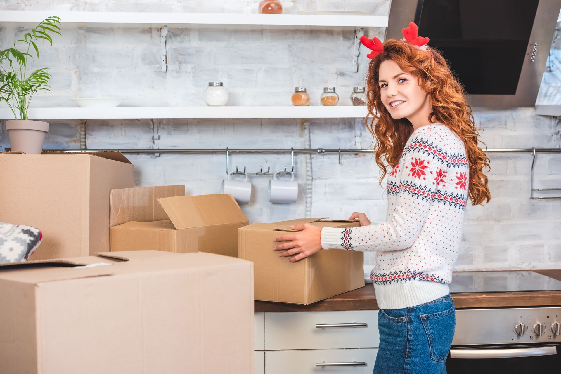 Woman in a Christmas sweater and antlers packing boxes in a kitchen.