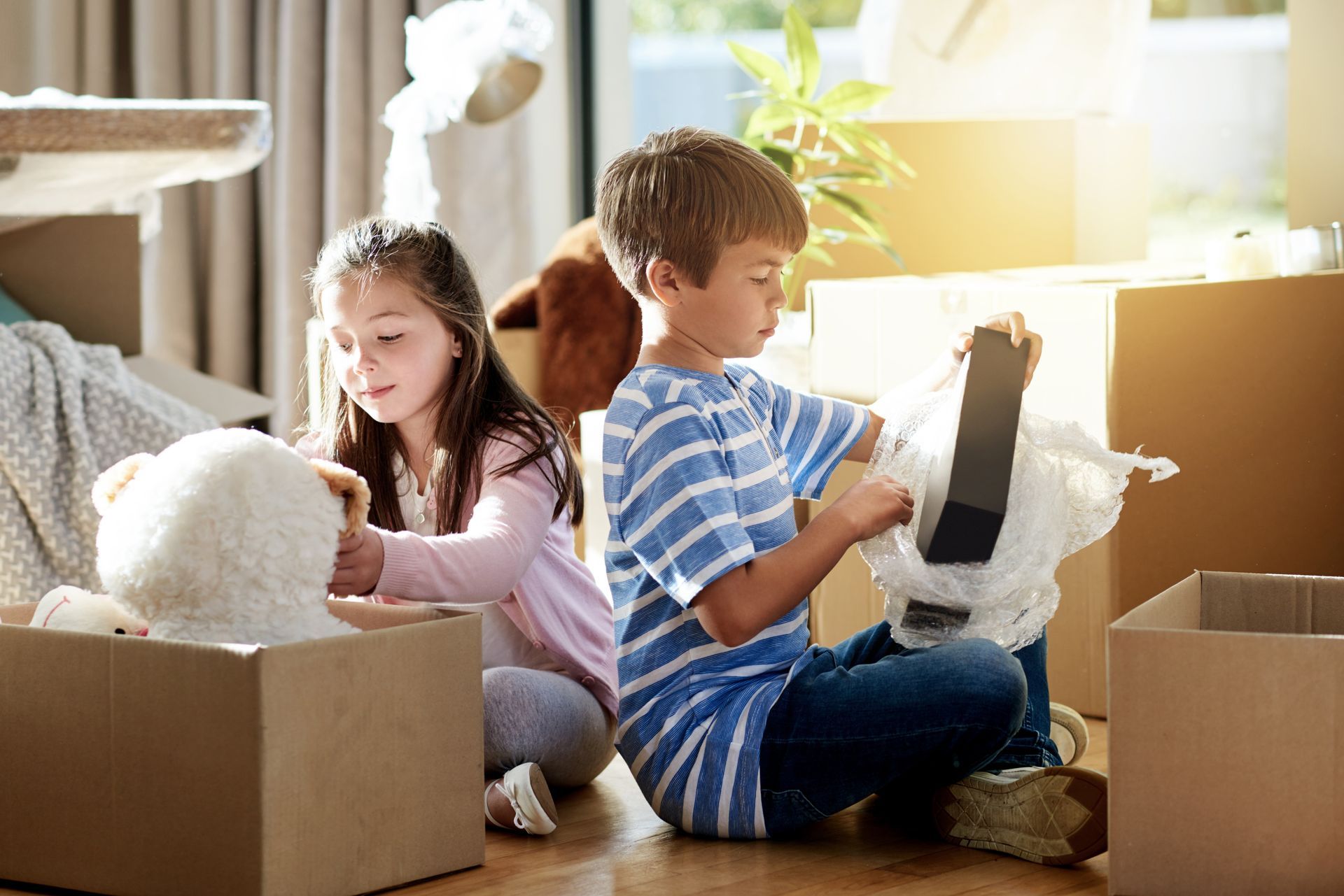 Two children unpacking boxes; girl with teddy bear, boy with stuffed dog.