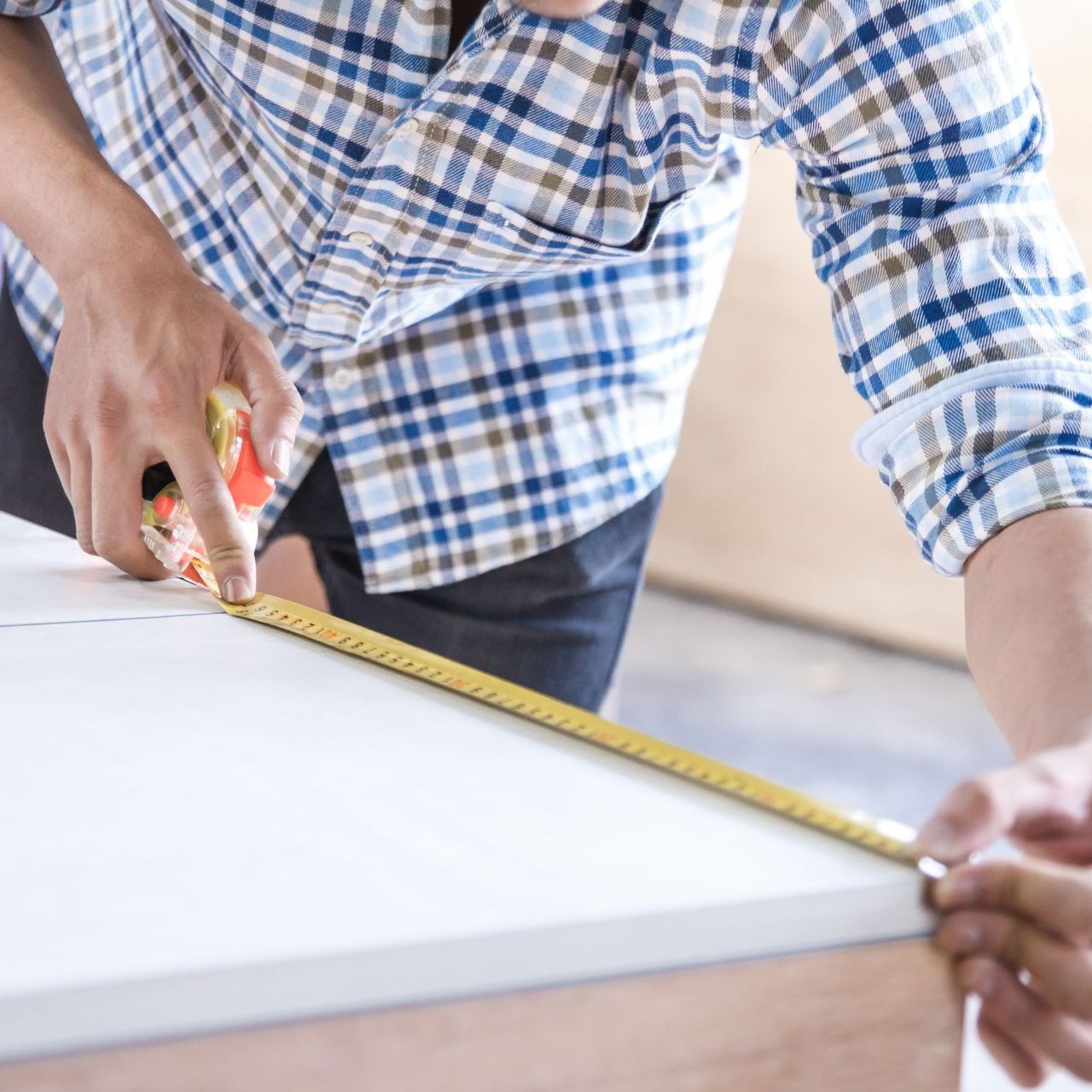 a man in a plaid shirt is measuring a table with a tape measure