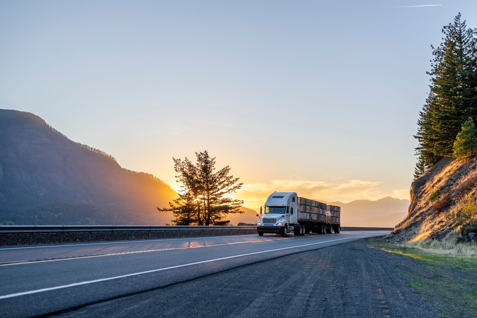 a semi truck is driving down a highway at sunset .
