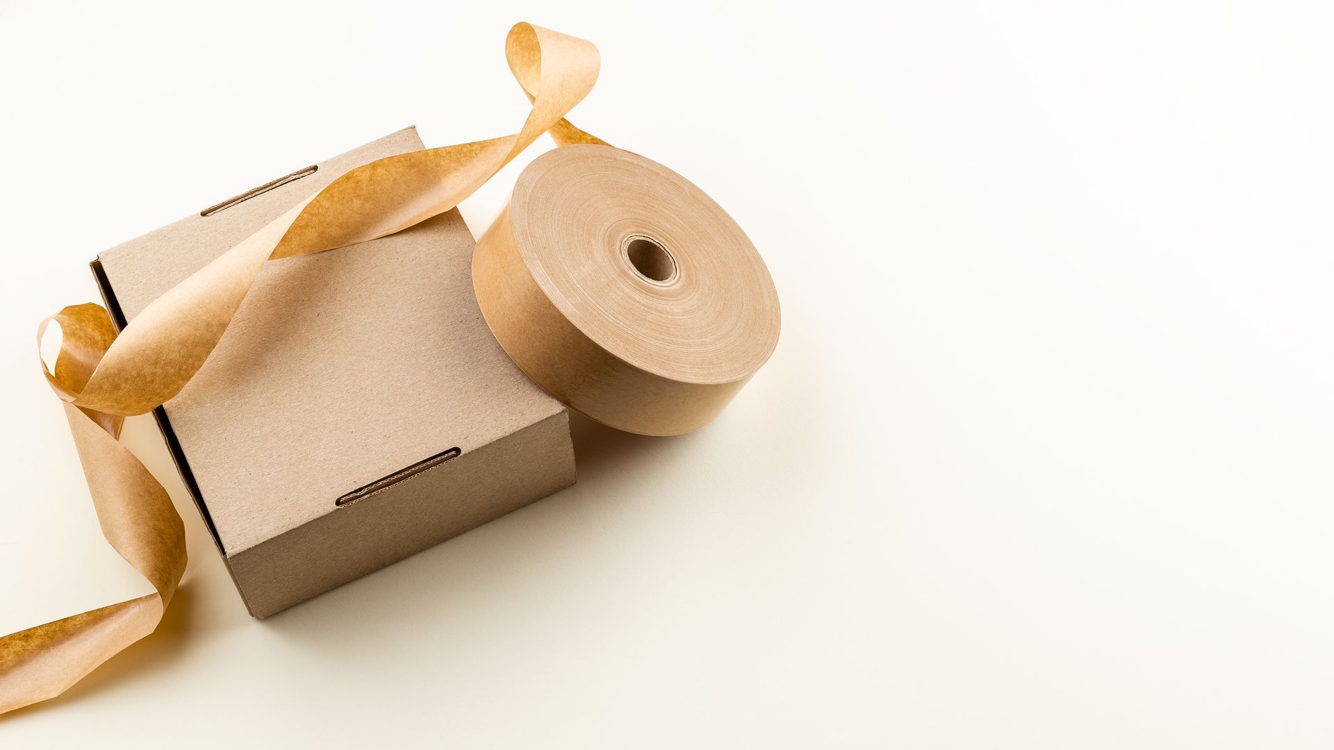 Two cardboard boxes and a roll of brown tape on a white surface.