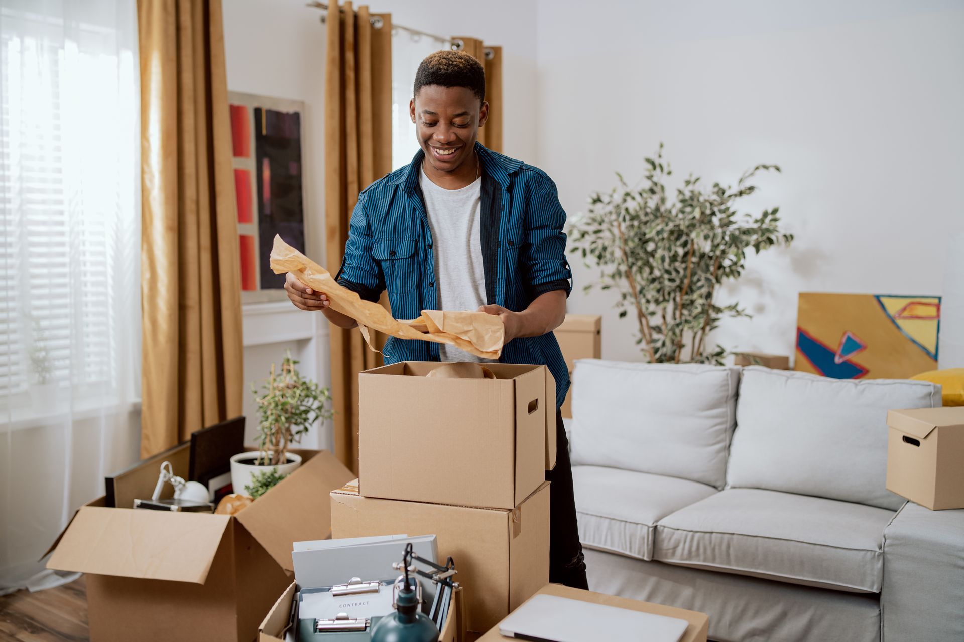 A man is standing in a living room surrounded by cardboard boxes.