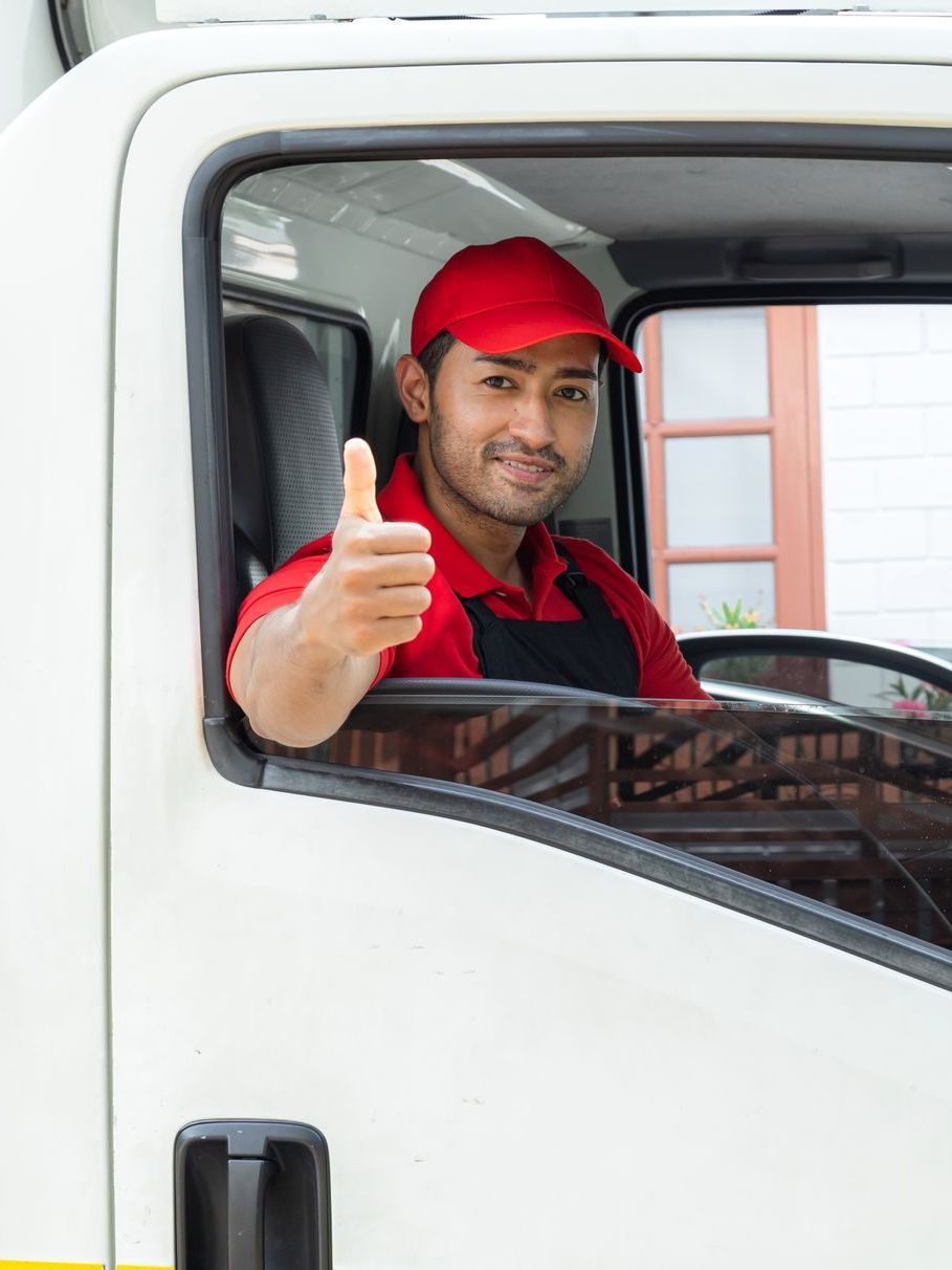 a delivery man is giving a thumbs up while sitting in the driver 's seat of a truck .