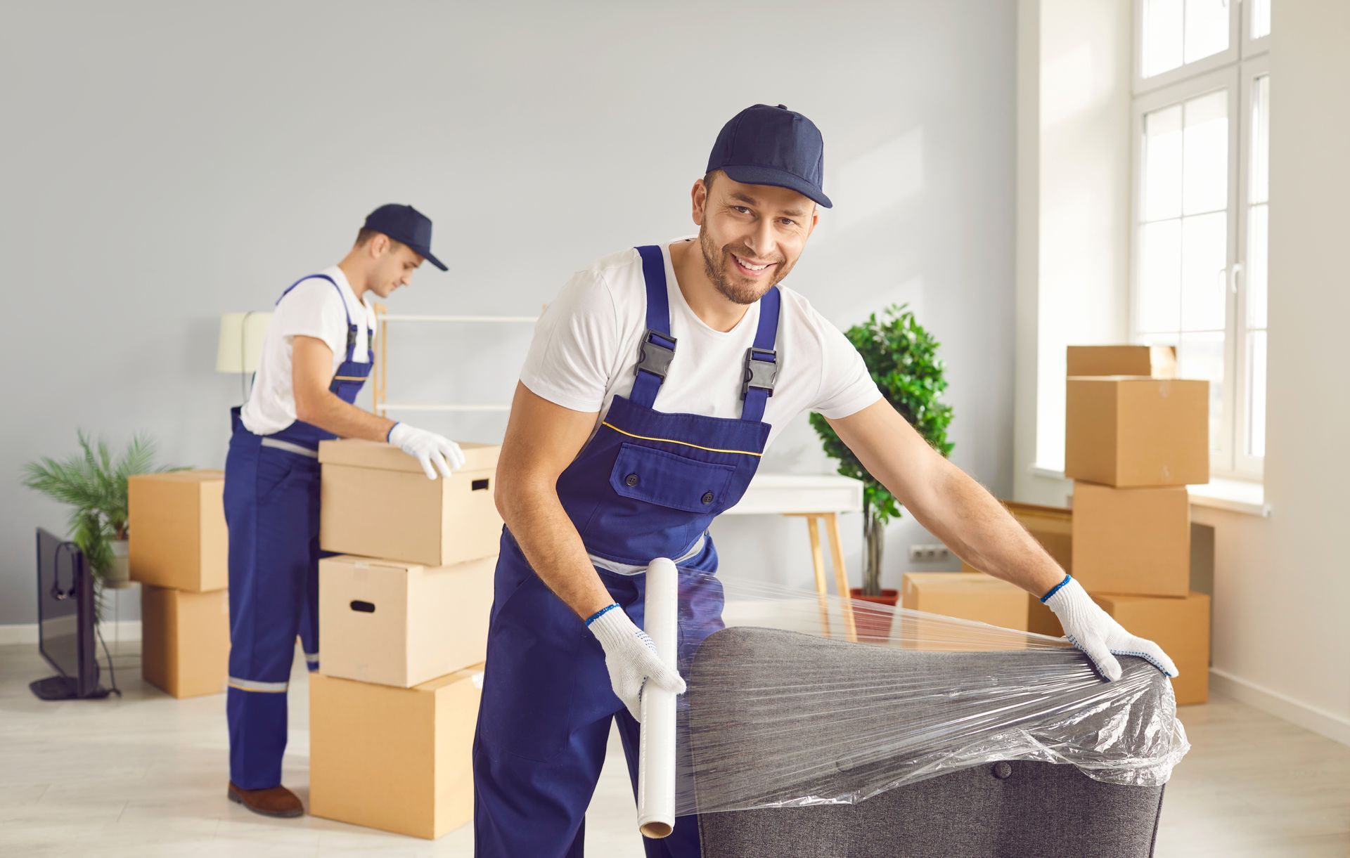 Two men are wrapping a couch in plastic wrap in a living room.