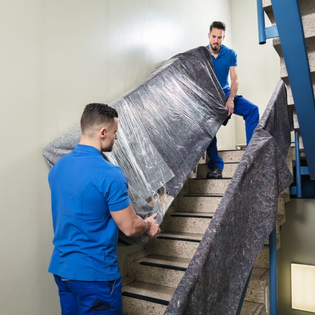 two men are moving a large piece of furniture up a set of stairs .