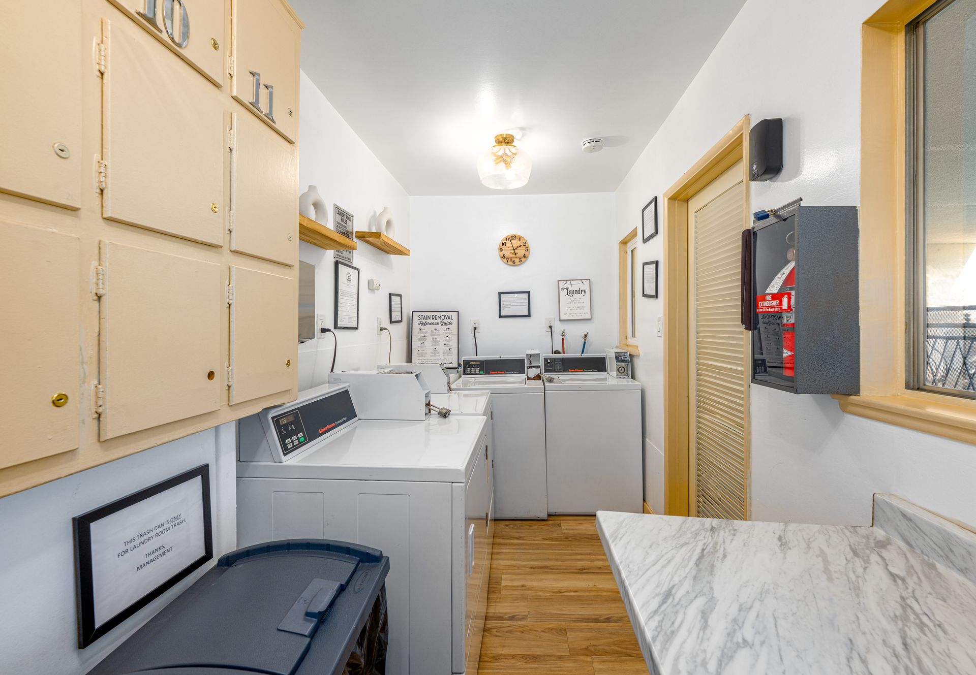 A small laundry room with white walls, wood floors, a washer and dryer, metal storage lockers, and a folding counter.