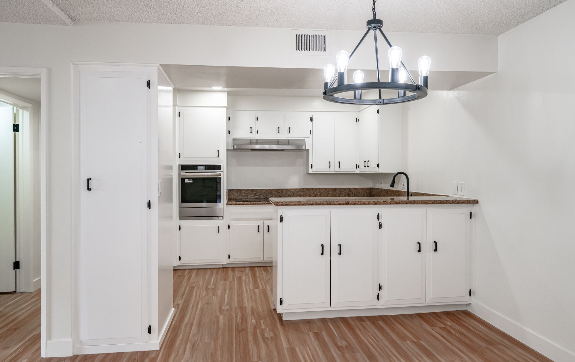 A bright kitchen featuring white cabinets, wood-look floors, a dark chandelier, and a breakfast bar counter.