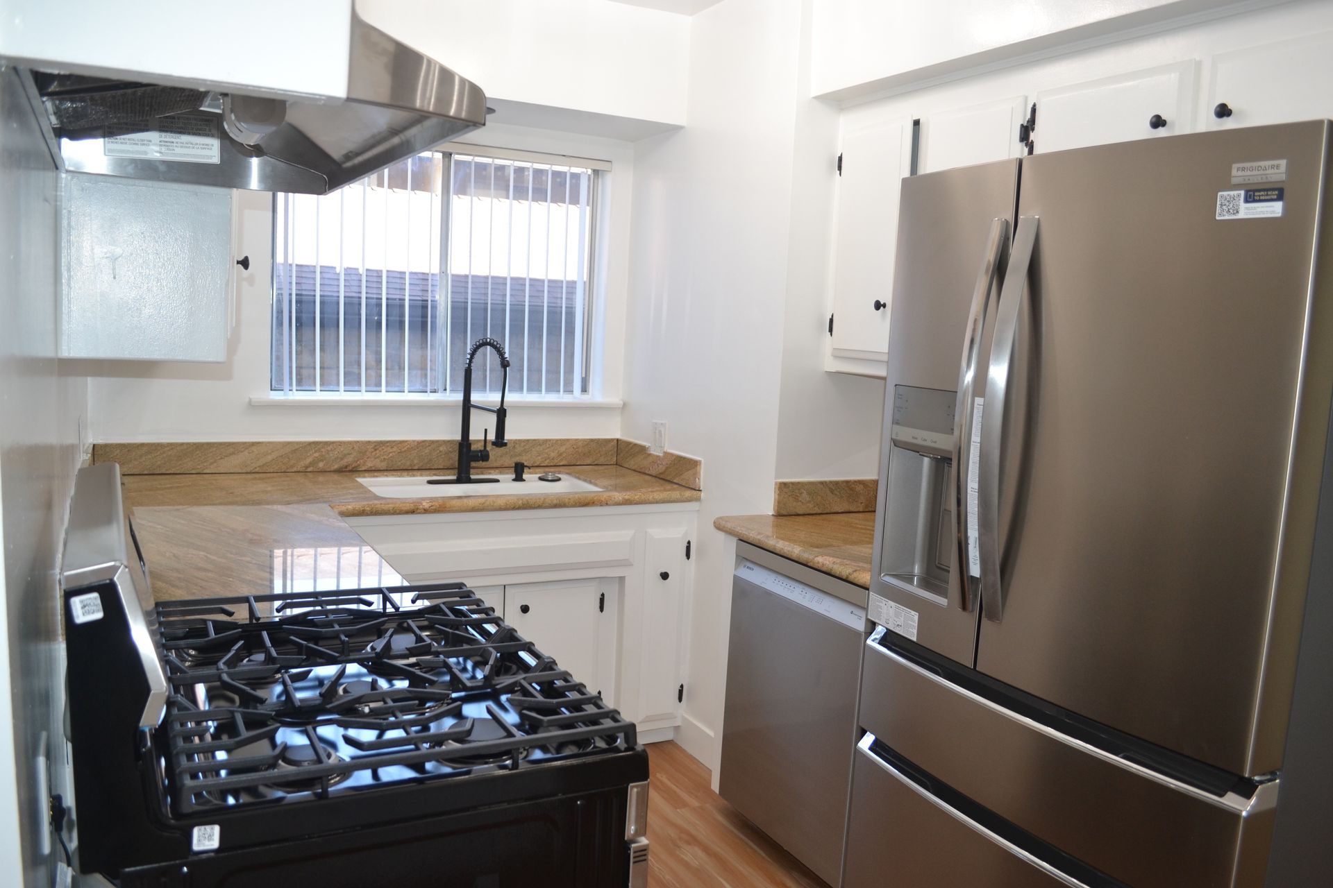 A modern kitchen featuring a stainless steel refrigerator, black gas stove, light-colored countertops, and white cabinets.