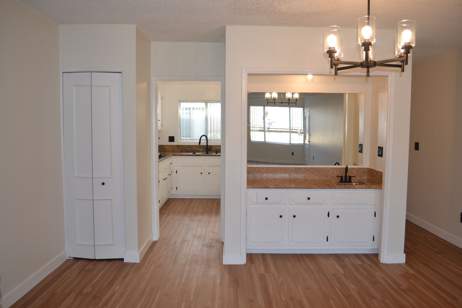 A kitchen and dining area with white cabinets, light wood flooring, a wet bar with a mirror, and a modern chandelier.