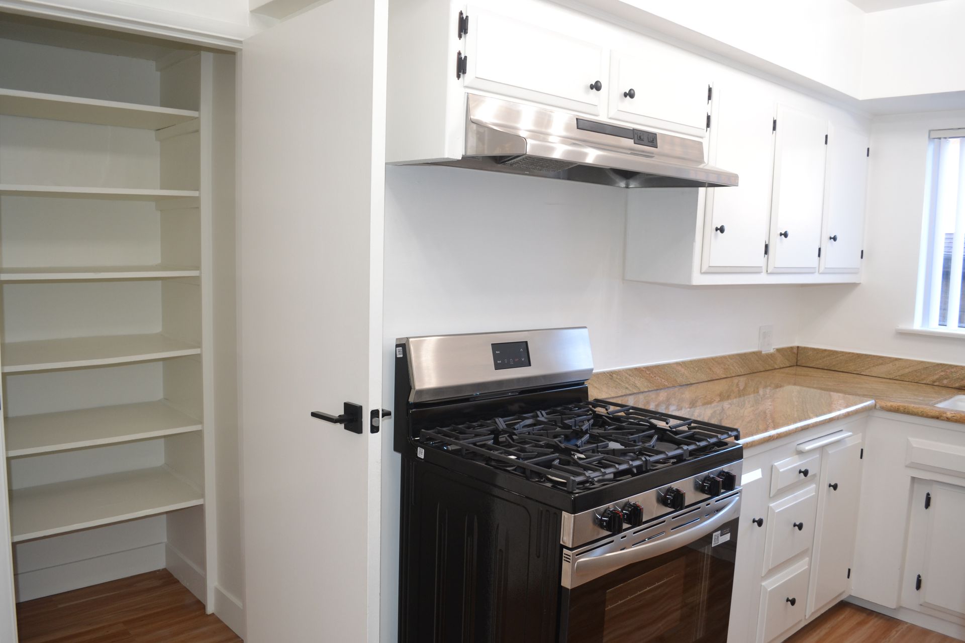 A kitchen view featuring a pantry with open shelves, a black gas stove with a metal hood, and white cabinets.