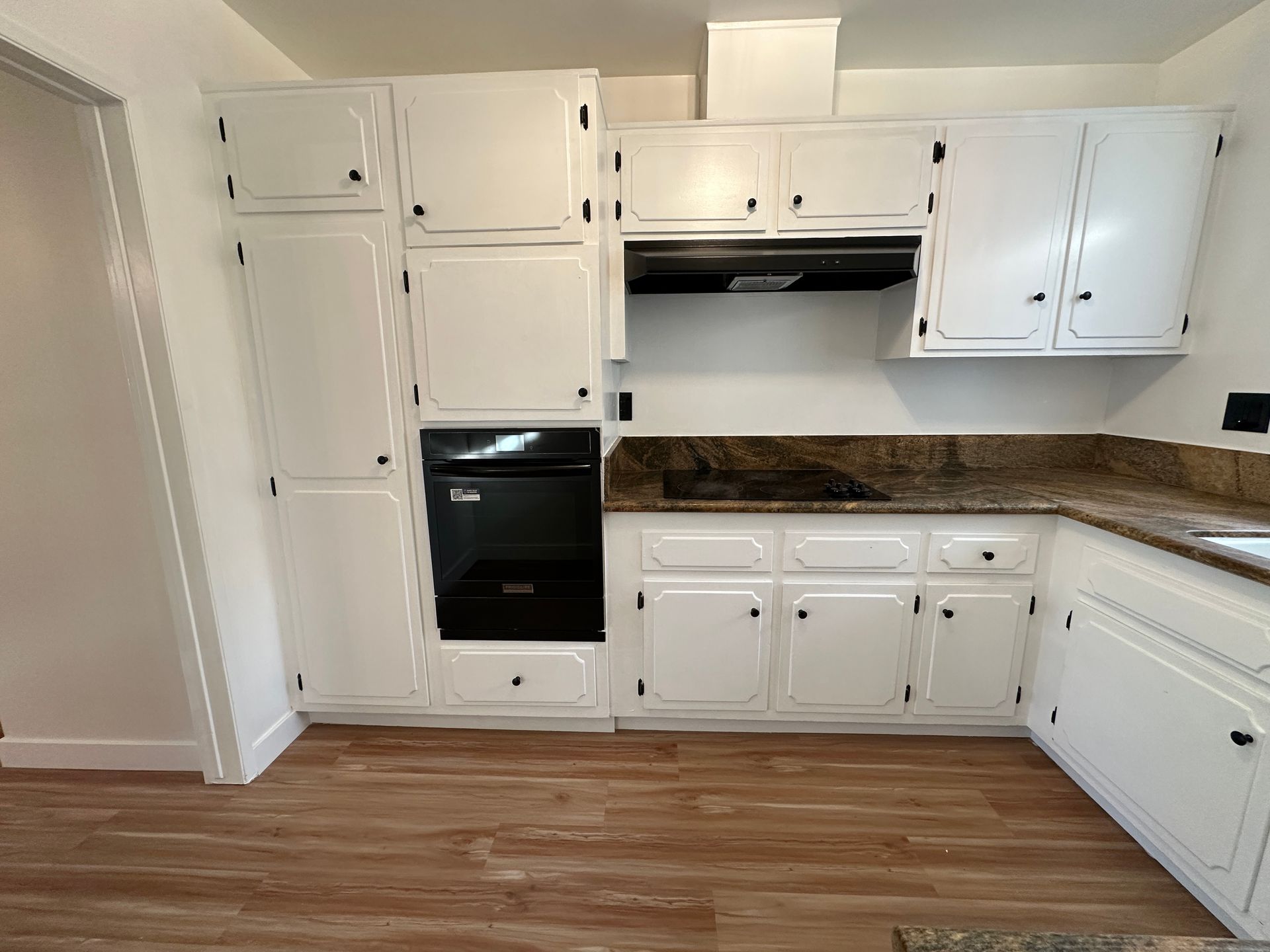 A brightly lit kitchen with white cabinets, a black built-in oven, and a dark brown granite countertop.