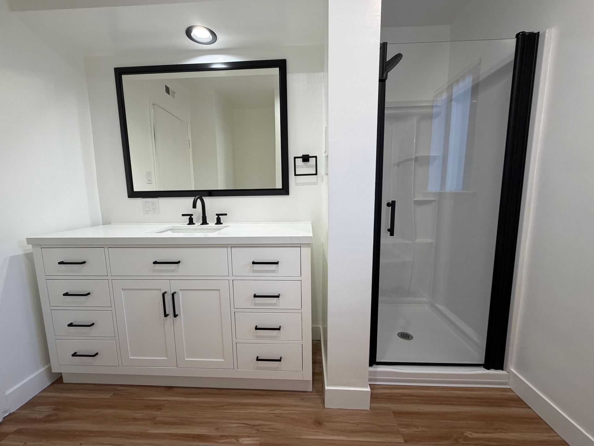 A modern bathroom featuring a white vanity with black hardware, a rectangular mirror, and a glass-enclosed shower.