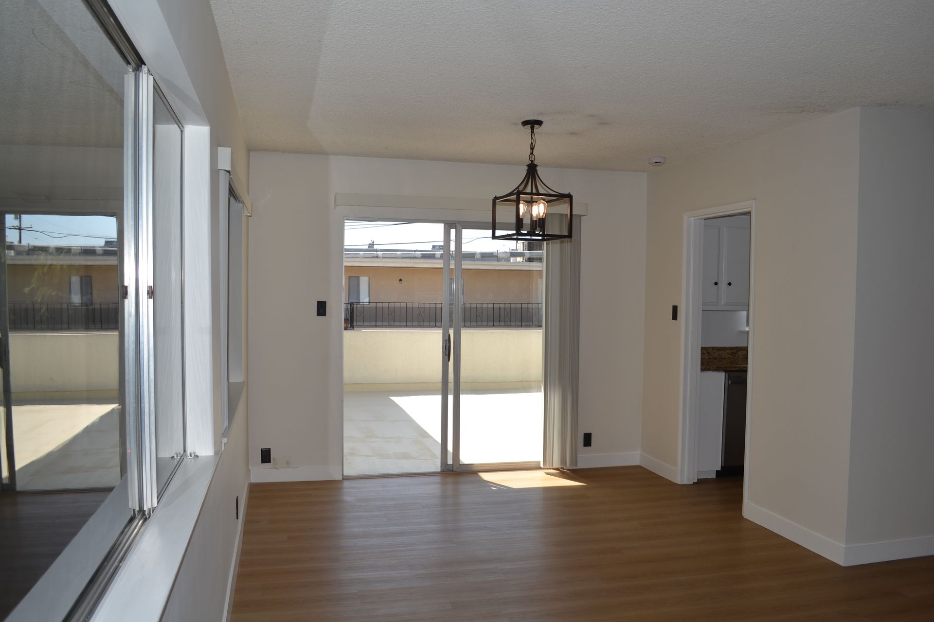 A brightly lit, empty dining area with light wood-style floors, a modern lantern-style chandelier, and glass sliding doors.