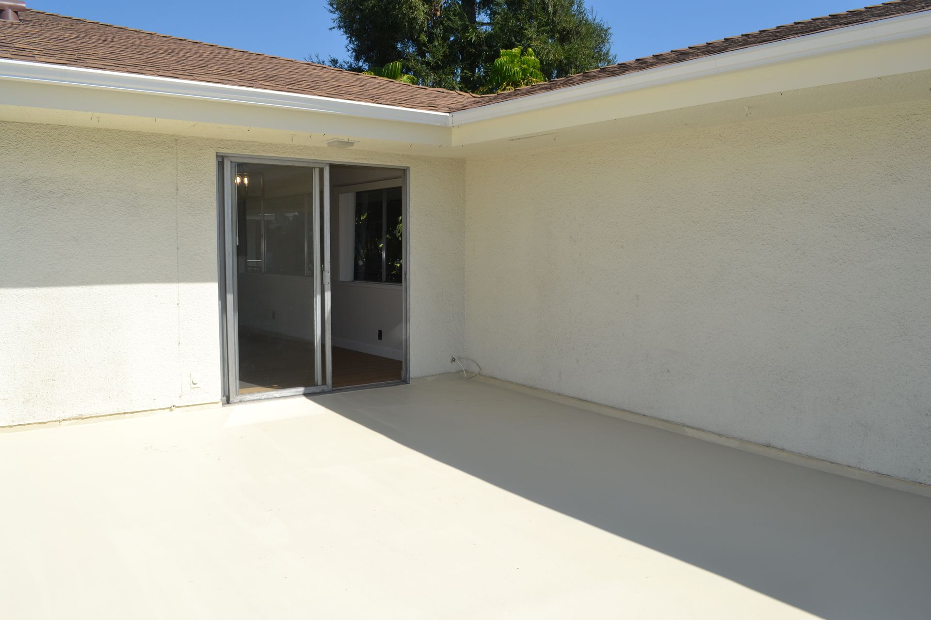 A beige patio area with a white stucco house exterior and a sliding glass door.