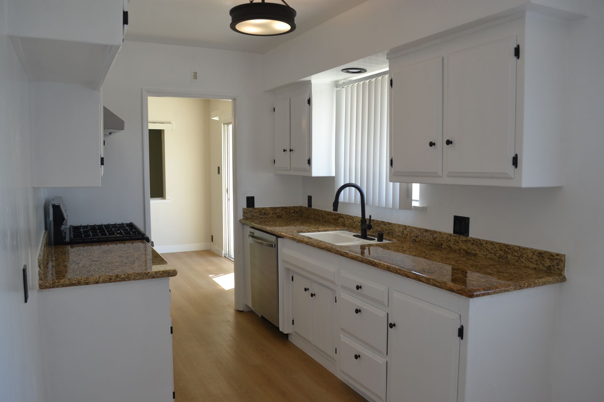 A white kitchen features granite countertops, a stainless steel dishwasher, and a dark faucet in front of a window.