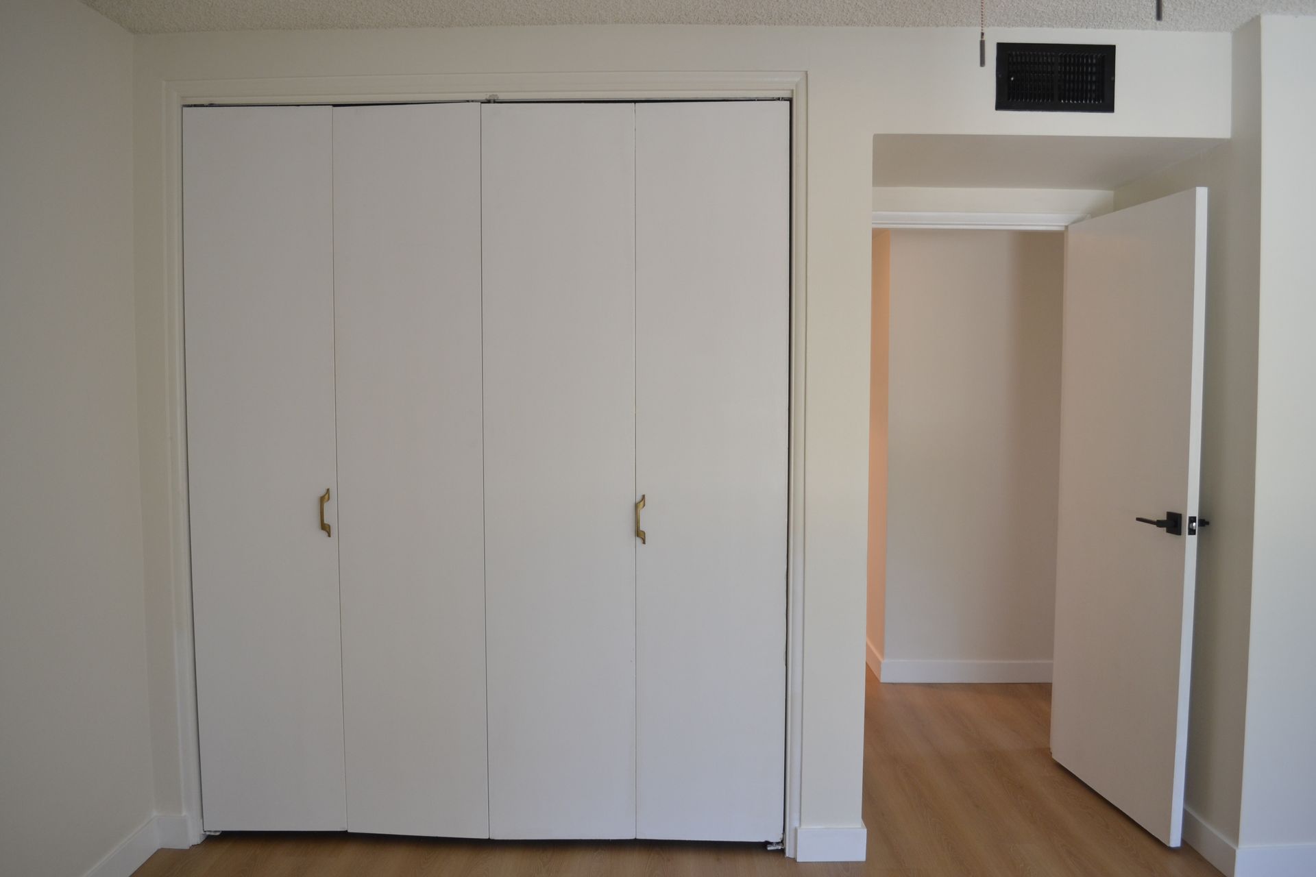A room featuring a white four-panel closet door next to an open doorway leading to an adjoining space with wood flooring.