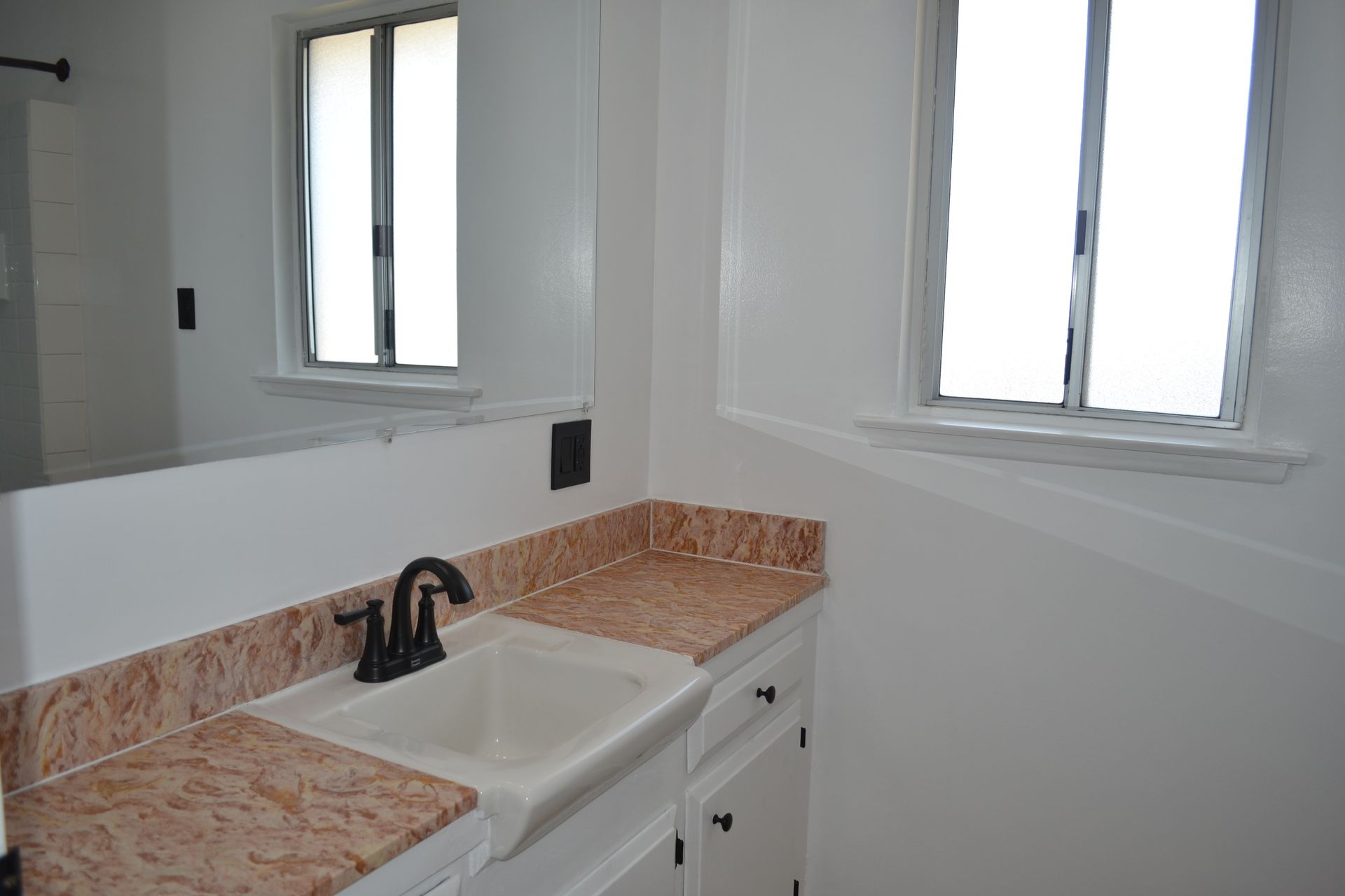 A bathroom vanity with a white sink, dark faucet, light wood-patterned countertop, and large mirror under a window.