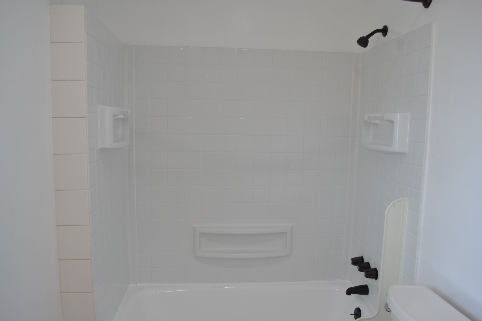 A white, tiled shower-tub surround with black fixtures and built-in niches for storage.