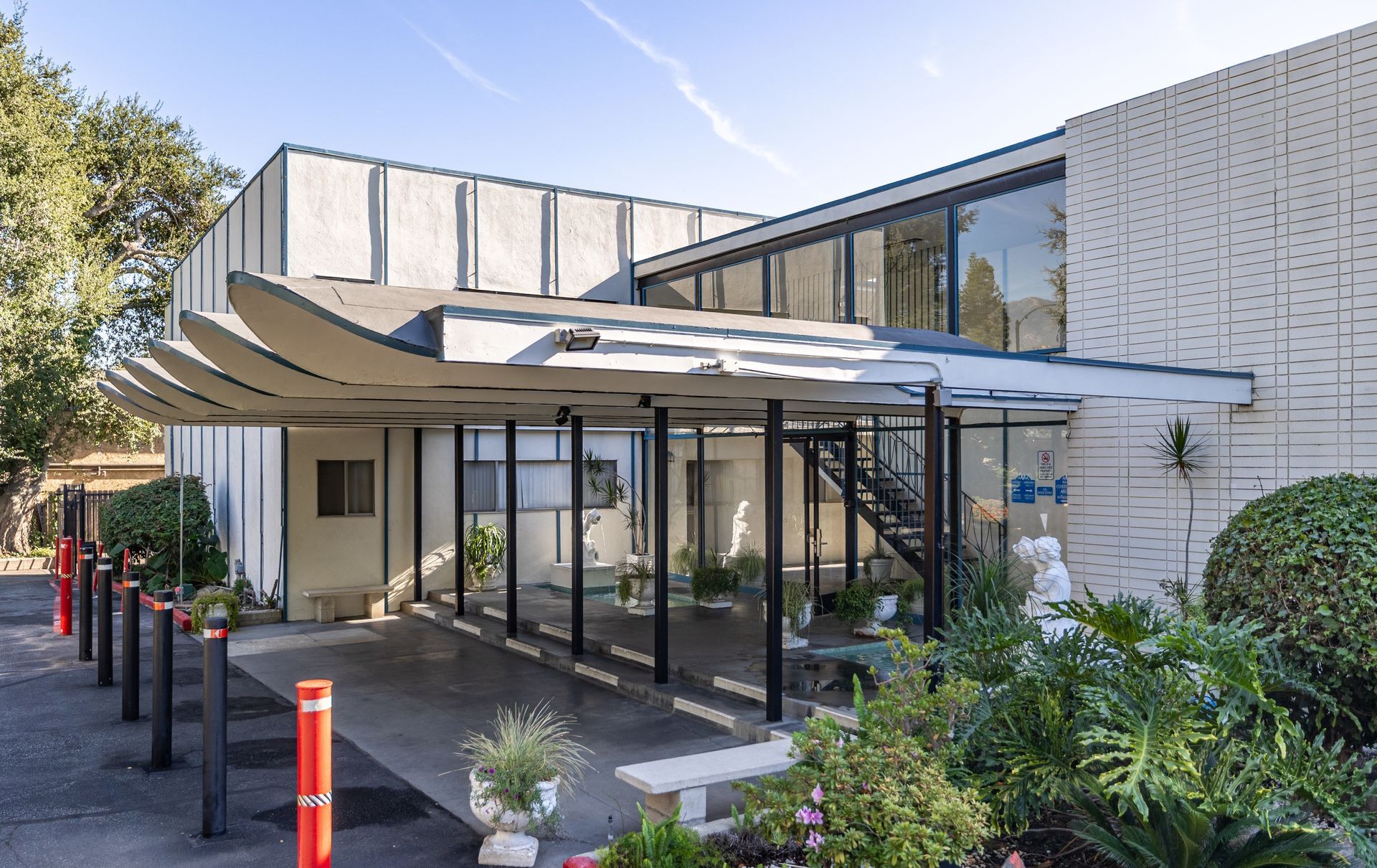A two-story building with a distinctive curved, multi-tiered awning over a paved entrance area, bordered by landscaping.