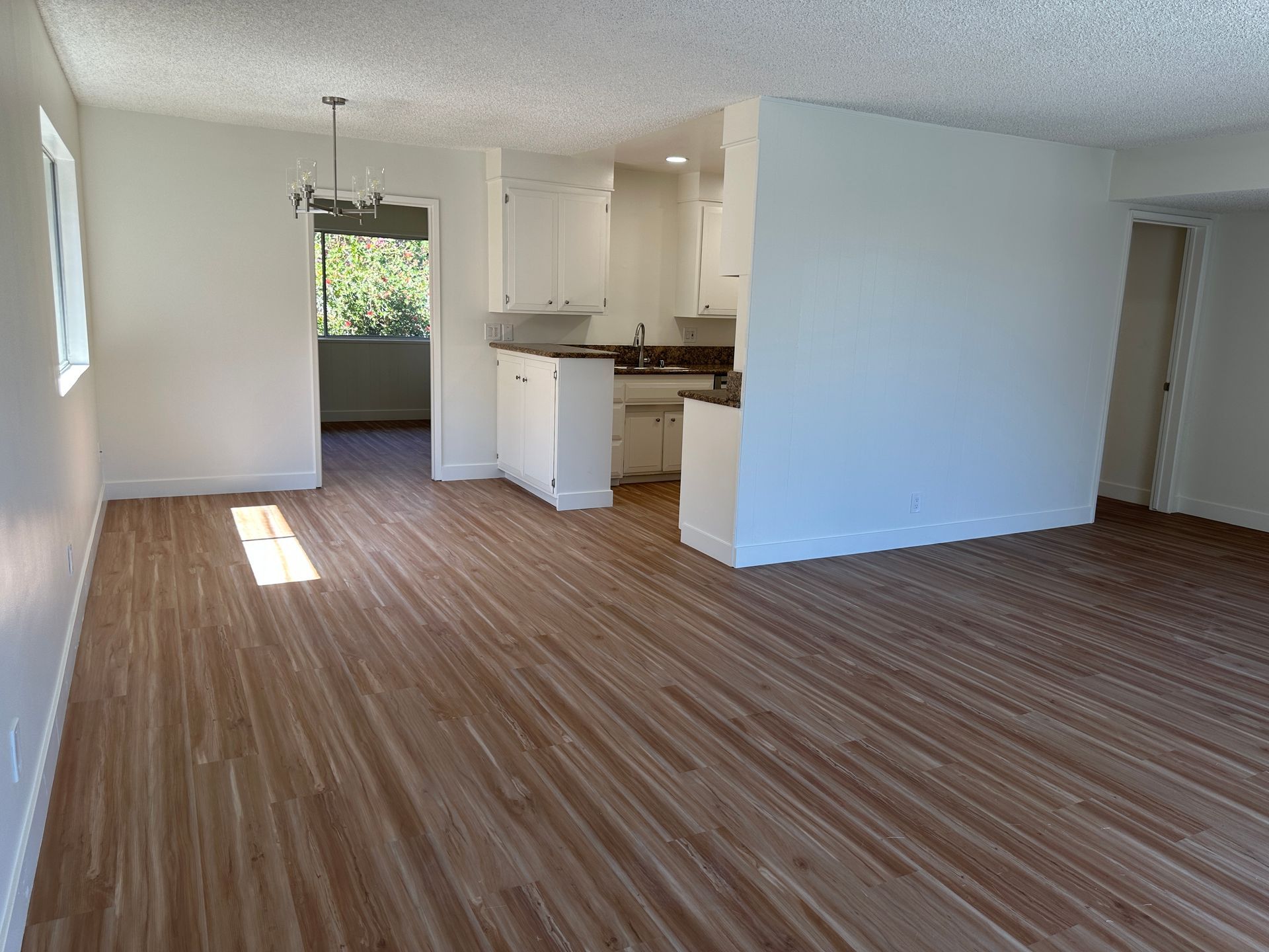 A wide-angle view of an empty apartment living and dining area featuring light wood-look floors, white walls, and kitchen.