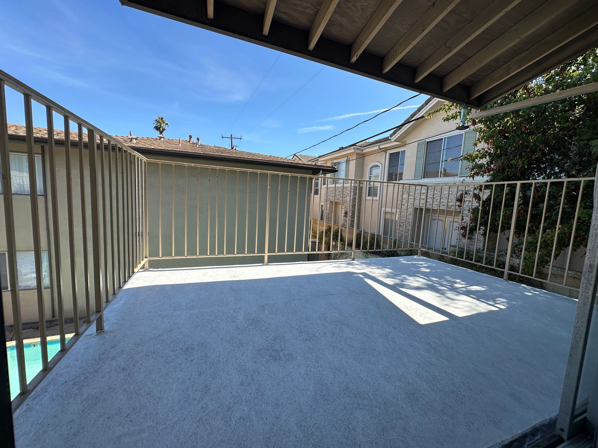 A wide-angle view of a flat, light-gray balcony deck enclosed by a metal railing, overlooking an apartment courtyard.