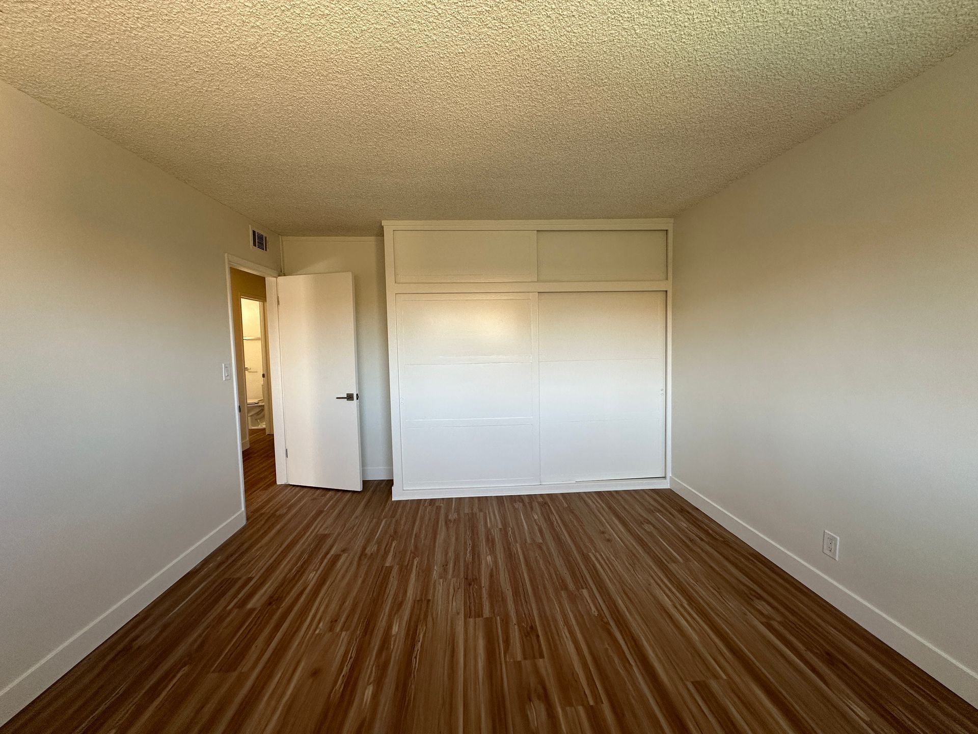 An empty room with light wood-look flooring, cream-colored walls, a ceiling with a popcorn texture, and a white closet.