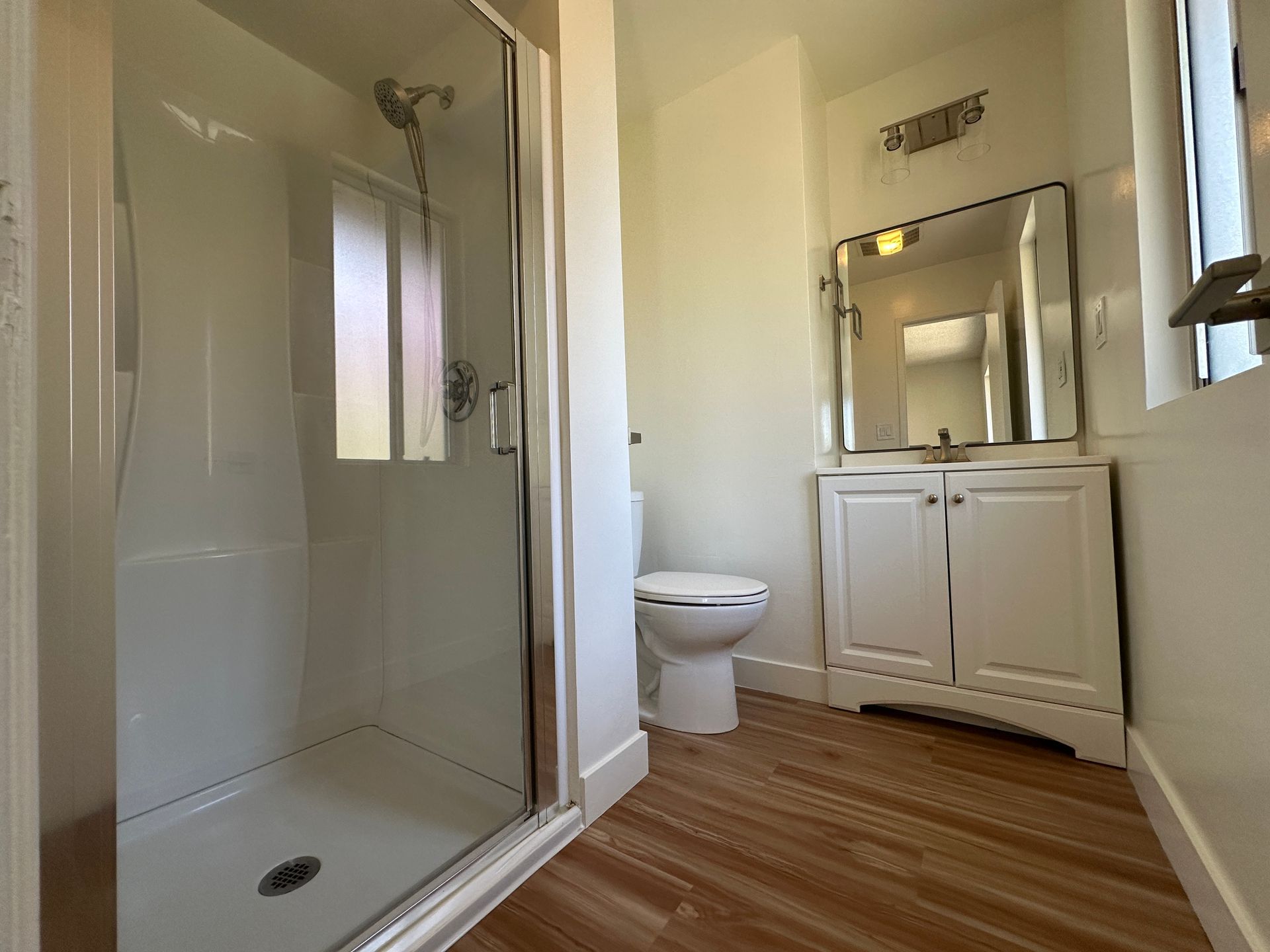 A bright, modern bathroom featuring a walk-in shower with glass doors, a white vanity with a mirror, and a toilet.