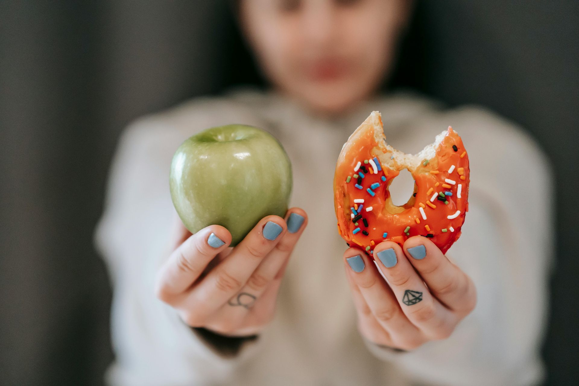 Person holding an apple and a donut with a bite taken from it