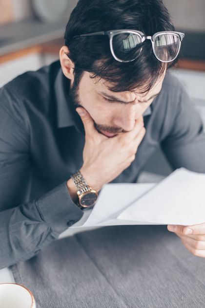 Person in black holding their head at a desk with papers and a calculator, looking stressed