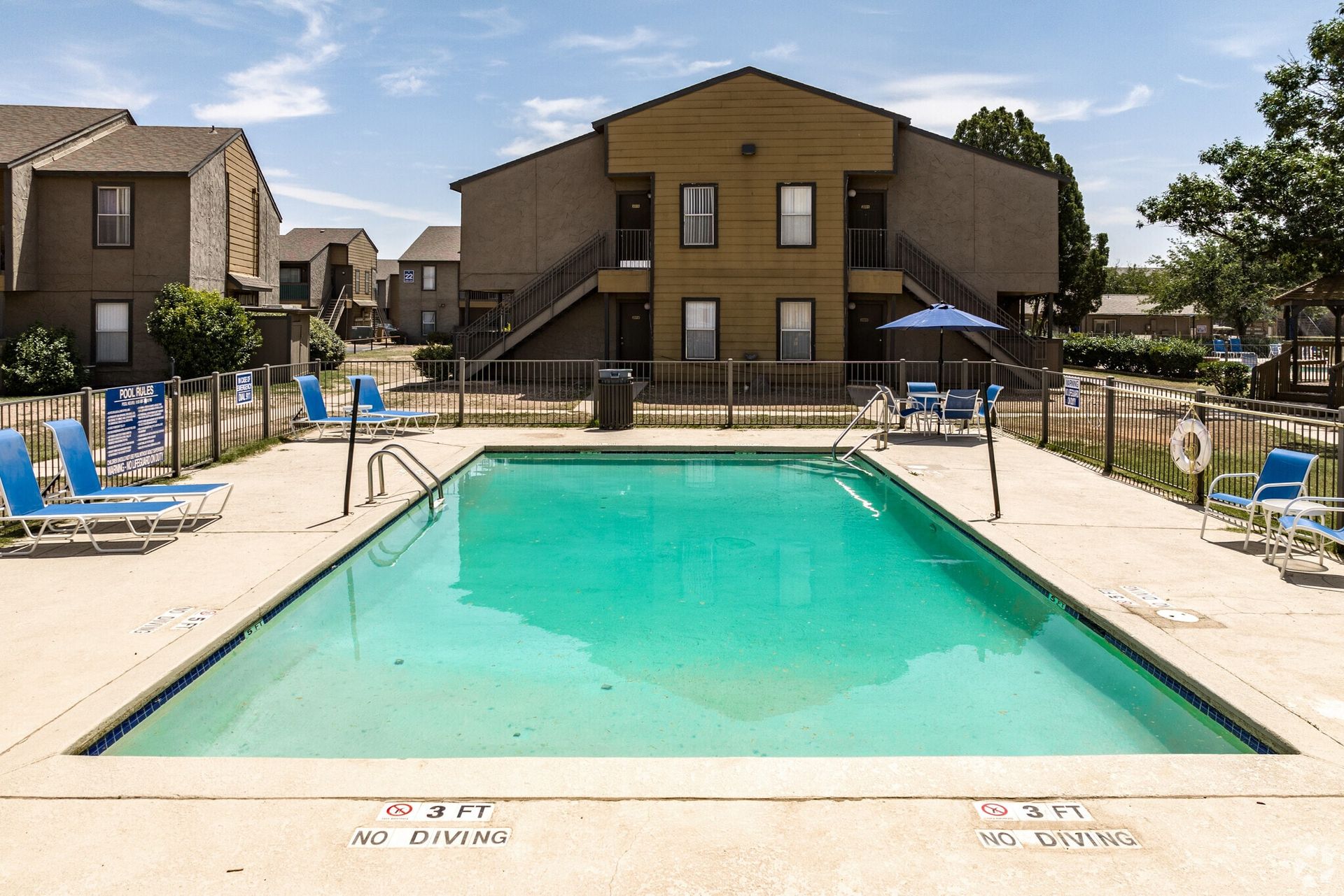 Pool surrounded by buildings with blue chairs and a sun umbrella.