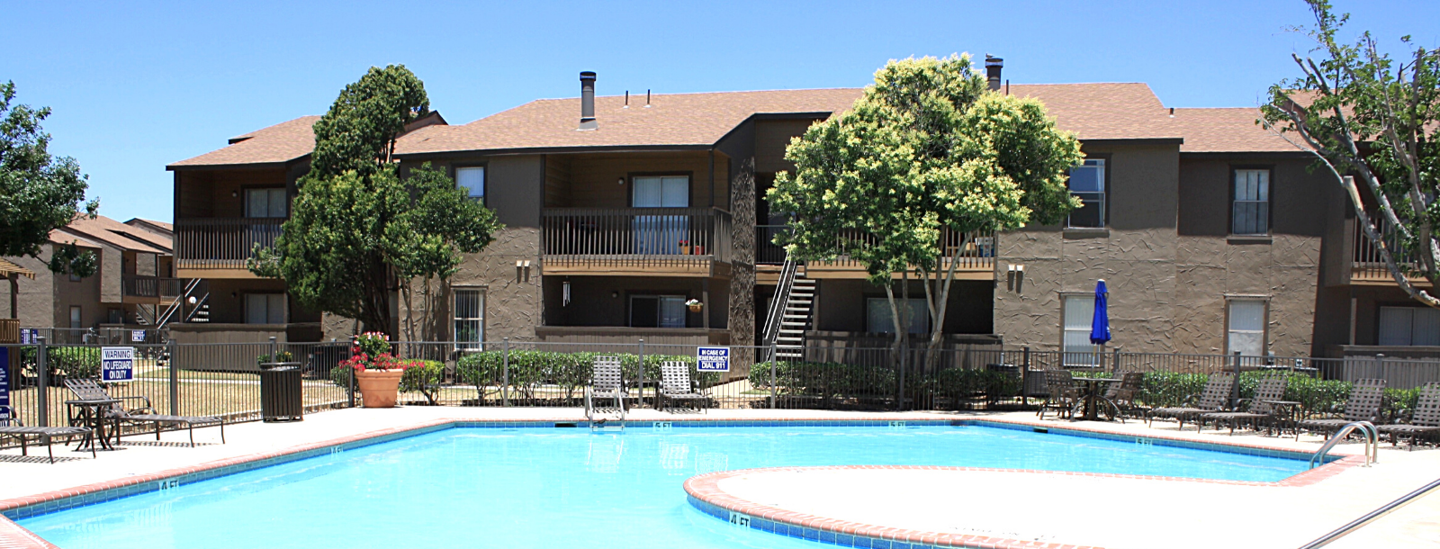 Outdoor pool with lounge chairs and apartment buildings in the background.