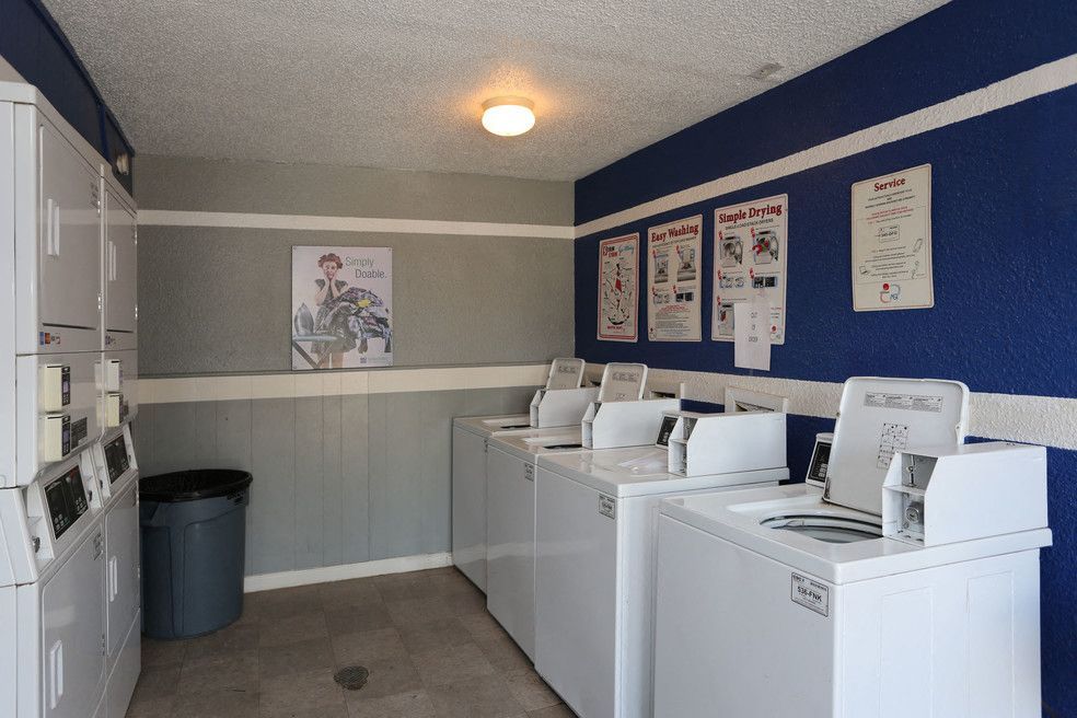 Community laundry room with multiple white washers and dryers along blue and gray walls.
