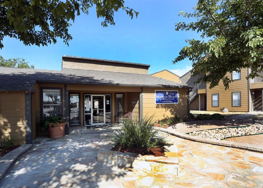 Exterior entrance to Madison Square apartment community with glass doors and landscaped walkway.