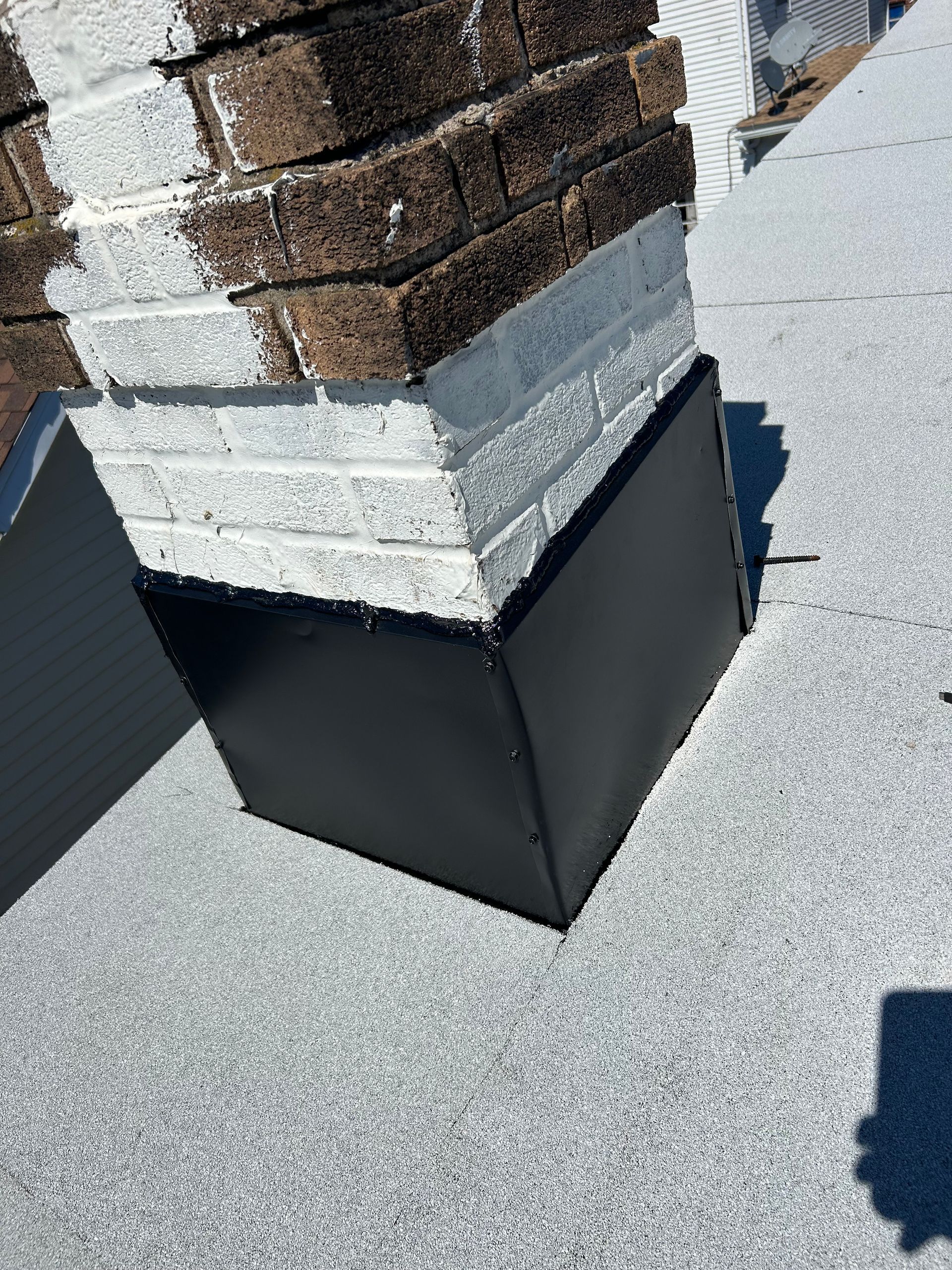 A black box is sitting next to a brick chimney on a roof