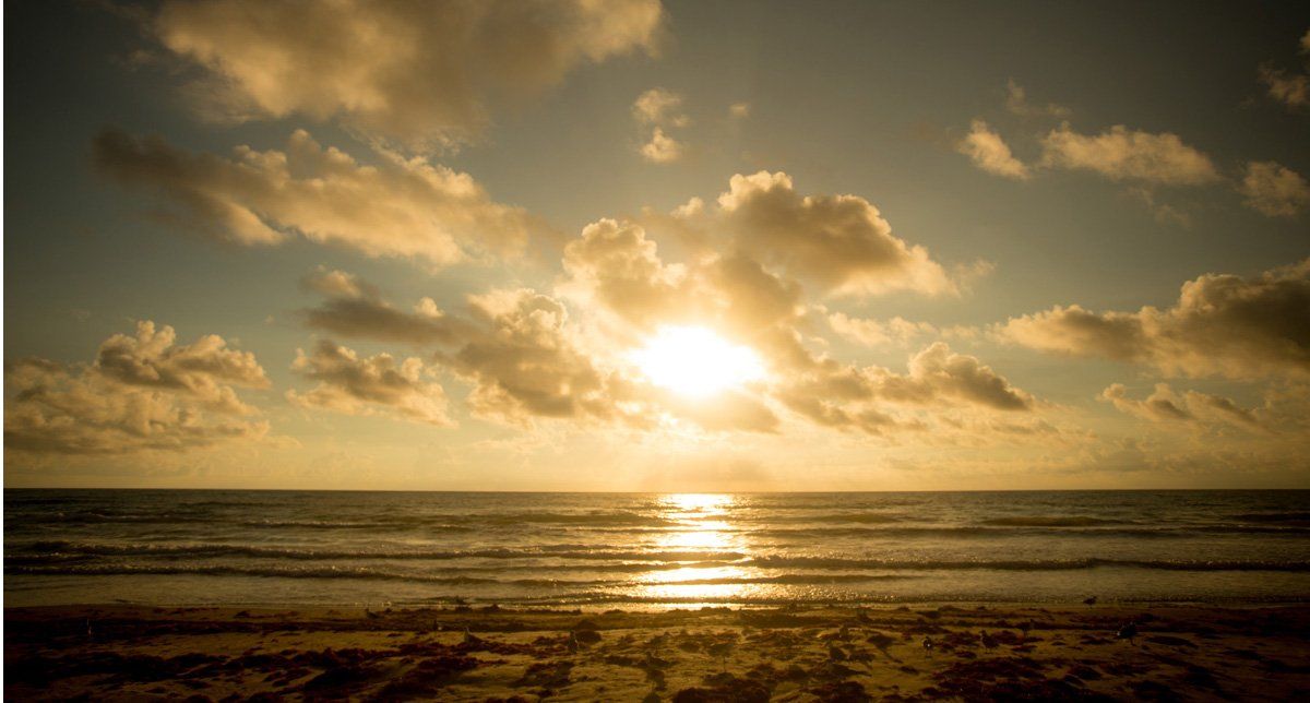 El sol se está poniendo sobre el océano con nubes en el cielo.