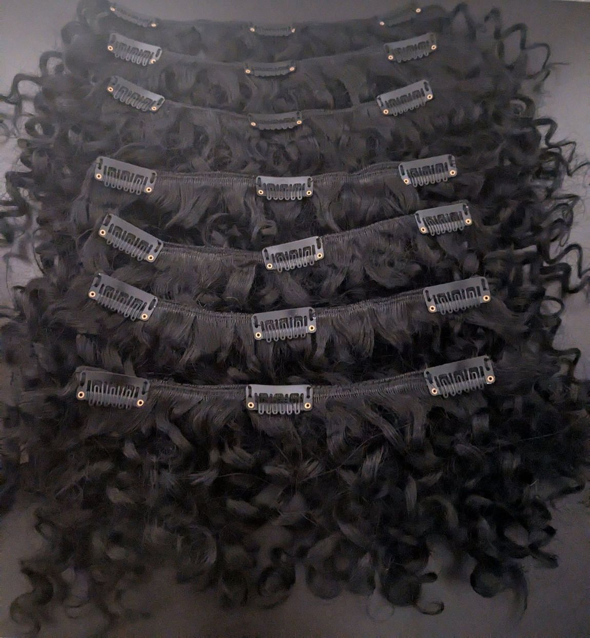 Black curly hair extensions with multiple clips arranged in a stack.