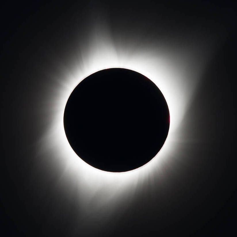 Total solar eclipse: Black sun surrounded by bright corona against a dark sky.