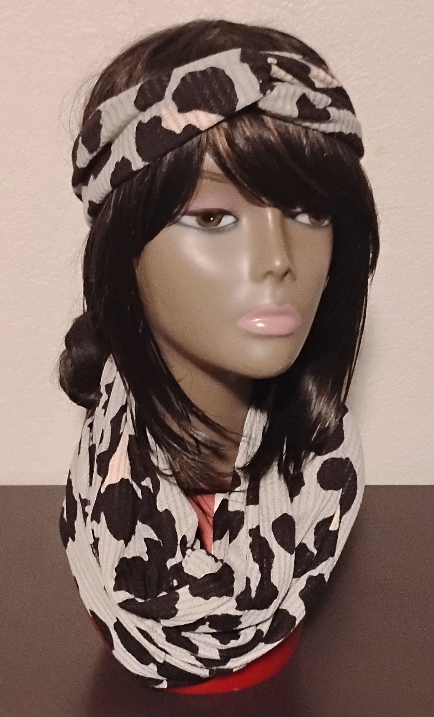 Mannequin head with a black wig, wearing a leopard print headband and infinity scarf.