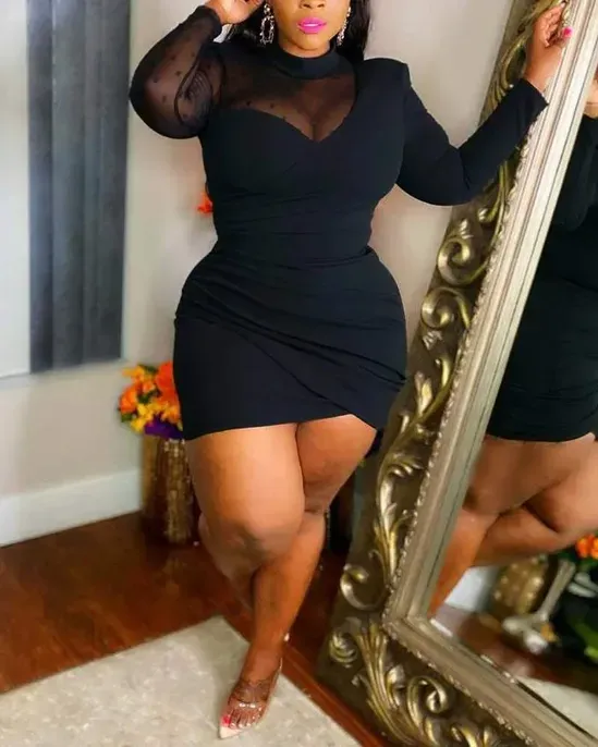 Woman in black dress poses near ornate mirror.