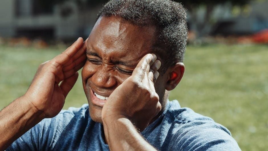 Person clutching their temples and grimacing outdoors on a sunny day