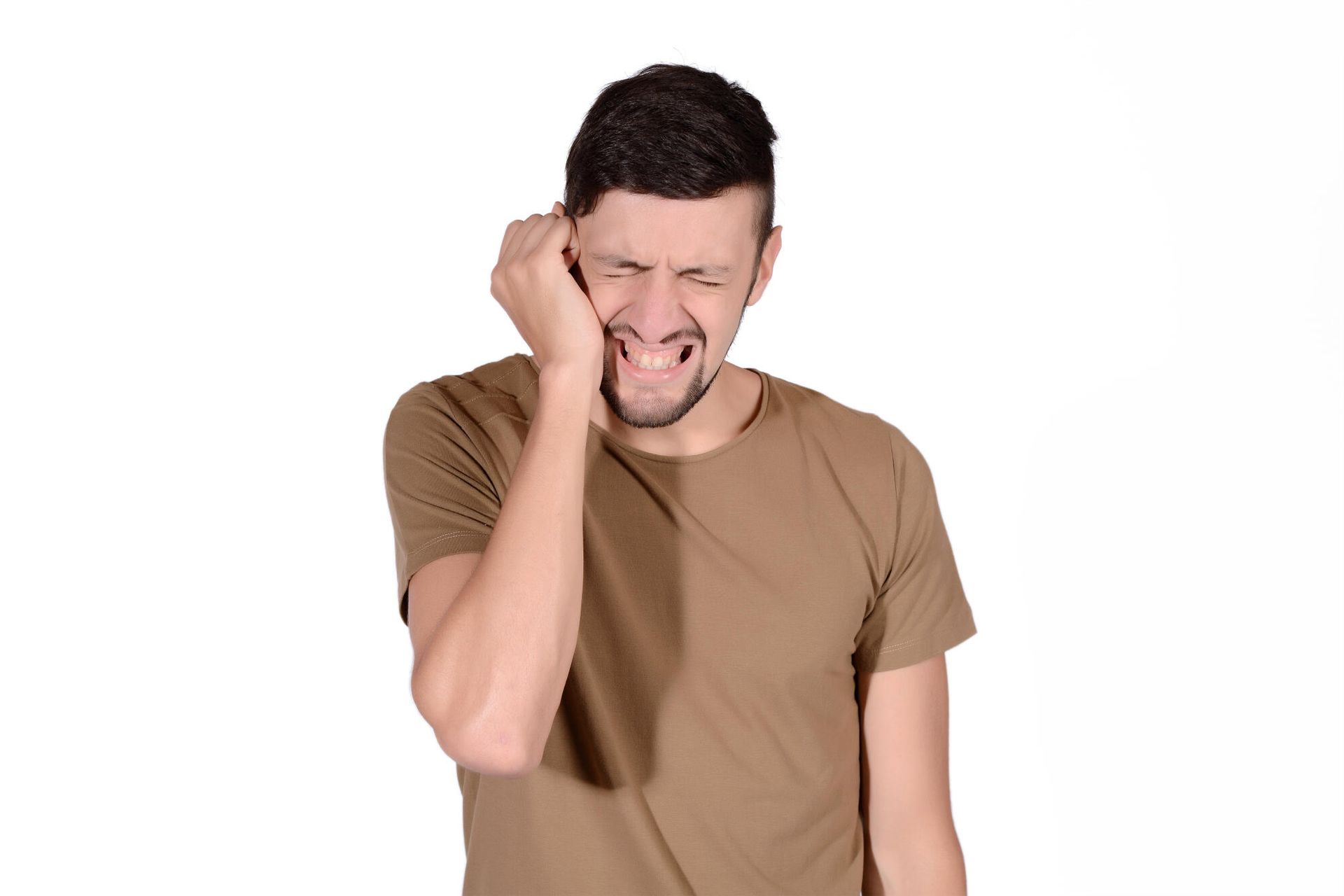 A person in a brown t-shirt grimacing in pain while holding their hand to their ear.