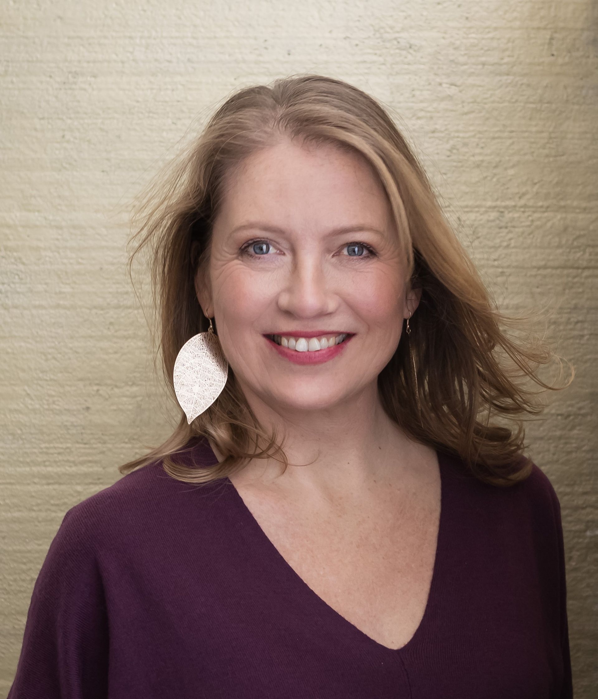 Een vrouw in pak en ketting lacht naar de camera.