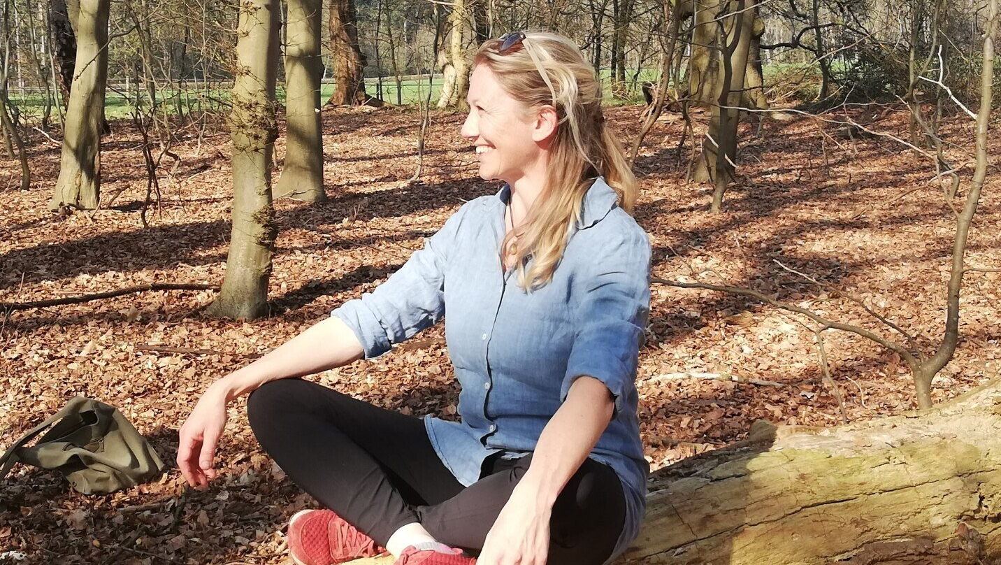 Een vrouw zit op de grond in het bos.